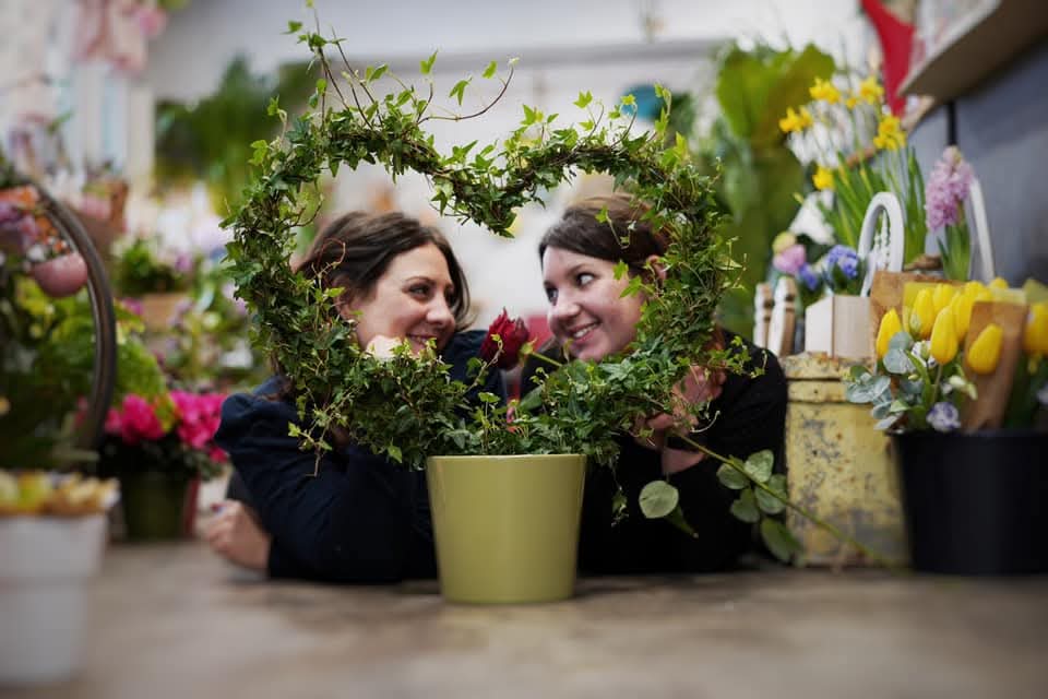 Les fleuristes à Arches, Pauline et Sabrina, qui se regardent en souriant au travers d'un plan de lierre en pot en forme de coeur