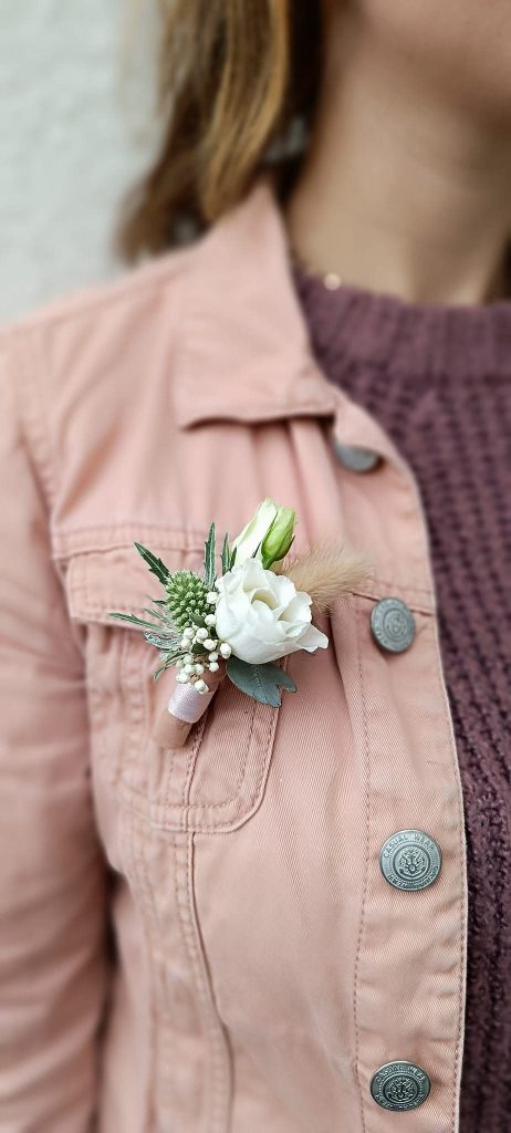 Une boutonnière de marié composé d'une petite rose blanche, portée sur la veste rose de la fleuriste Sabrina