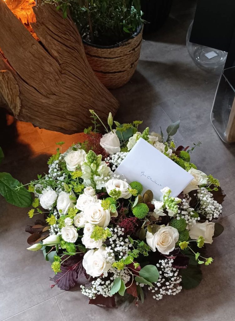 Une gerbe de fleurs réalisée pour un deuil, composée de roses blanche, gypsophile et feuillage vert
