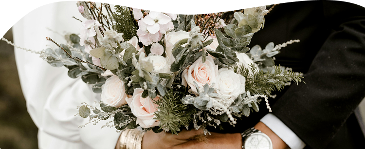Bouquet de mariée tenu par le couple, on aperçoit la mariée qui est habillée en blanc et le marié en noir