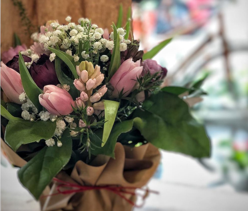 Un bouquet de fleurs rose et blanc, composé de tulipes et de gypsophiles, avec du feuillage et emballé dans du papier kraft
