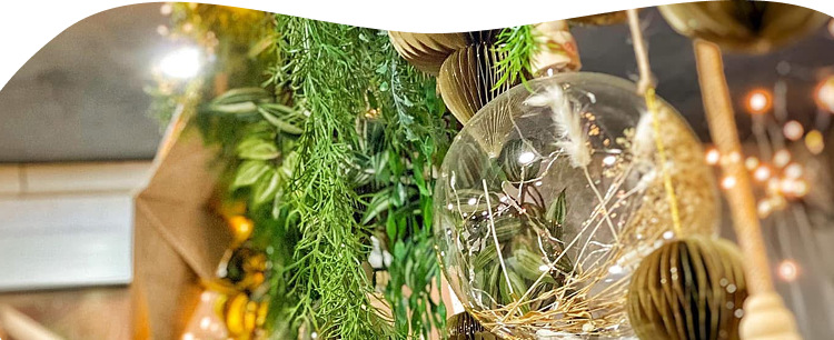 Photo zoome sur un ensemble de décoration suspendue végétale, avec une boule en verre et des guirlandes lumineuses