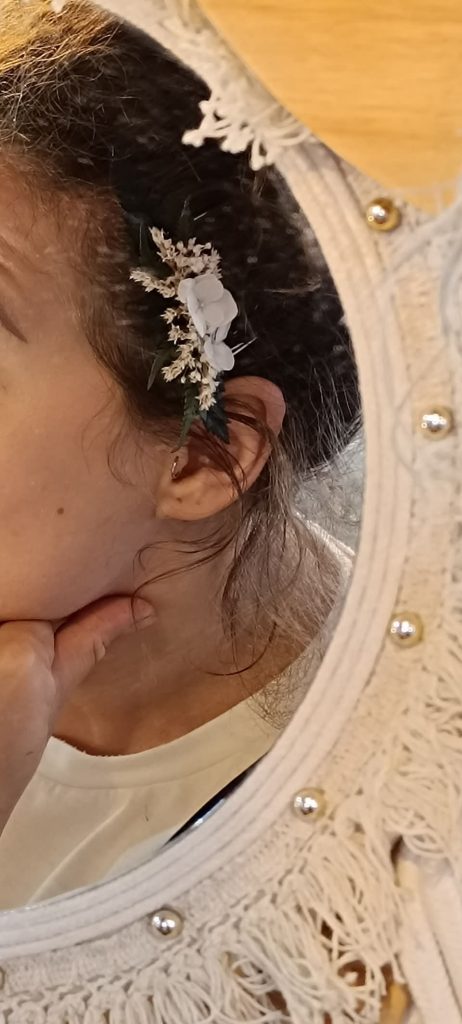 La fleuriste Pauline est devant un miroir avec un barrette fleurie crée sur mesure dans les tons blancs