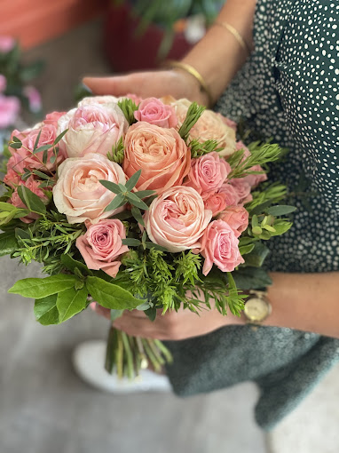 Les mains de fleuriste tiennent un joli bouquet de roses fraîches avec du feuillage vert pour un baptême à Arches