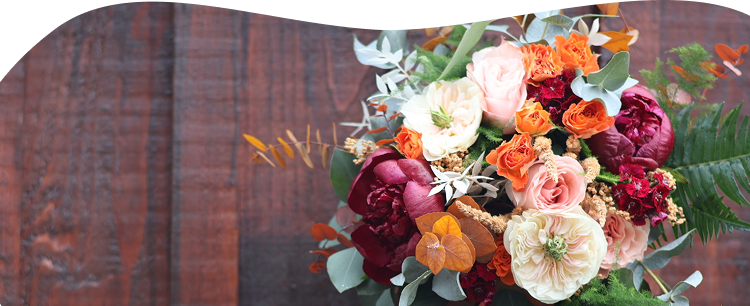 Un joli bouquet de fleurs coloré orange, bordeaux et vert placé sur un fond en bois foncé