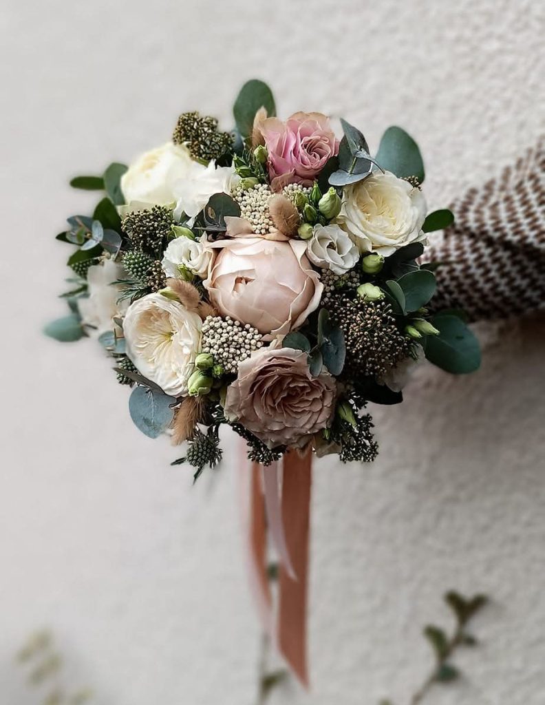 Un bouquet de mariée dans des tons très doux rose pastel et vert, attaché par un ruban rose qui retombe