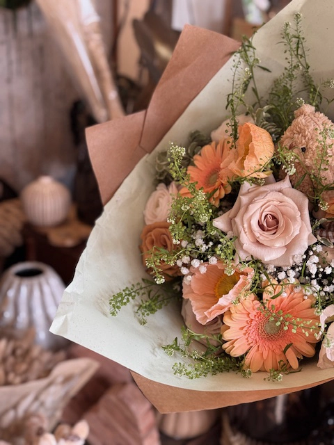 Un bouquet de fleurs rose et orange emballé dans du papier kraft et papier de soie assortit