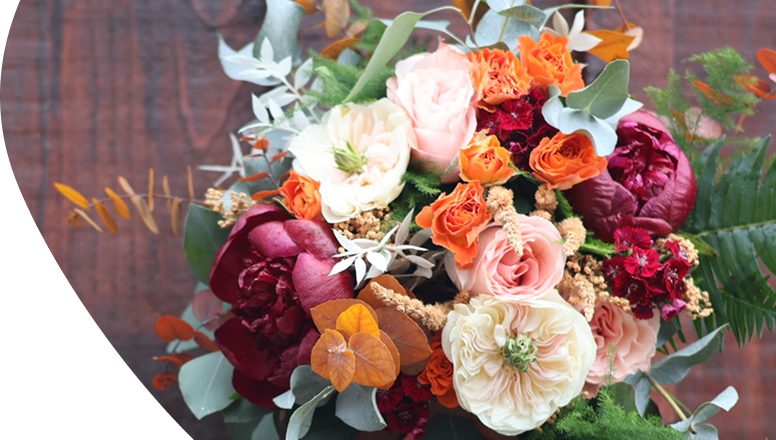 Un bouquet de fleurs sur mesure orange et rose très coloré placé devant un fond en bois foncé