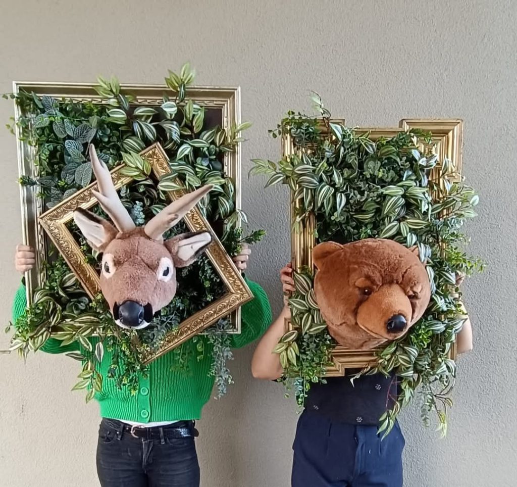 Les fleuristes ont réalisé une décoration pour entreprise composé de deux cadres végétaux originaux avec des têtes de peluches de cerf et d'ours et les portent devant leurs visages