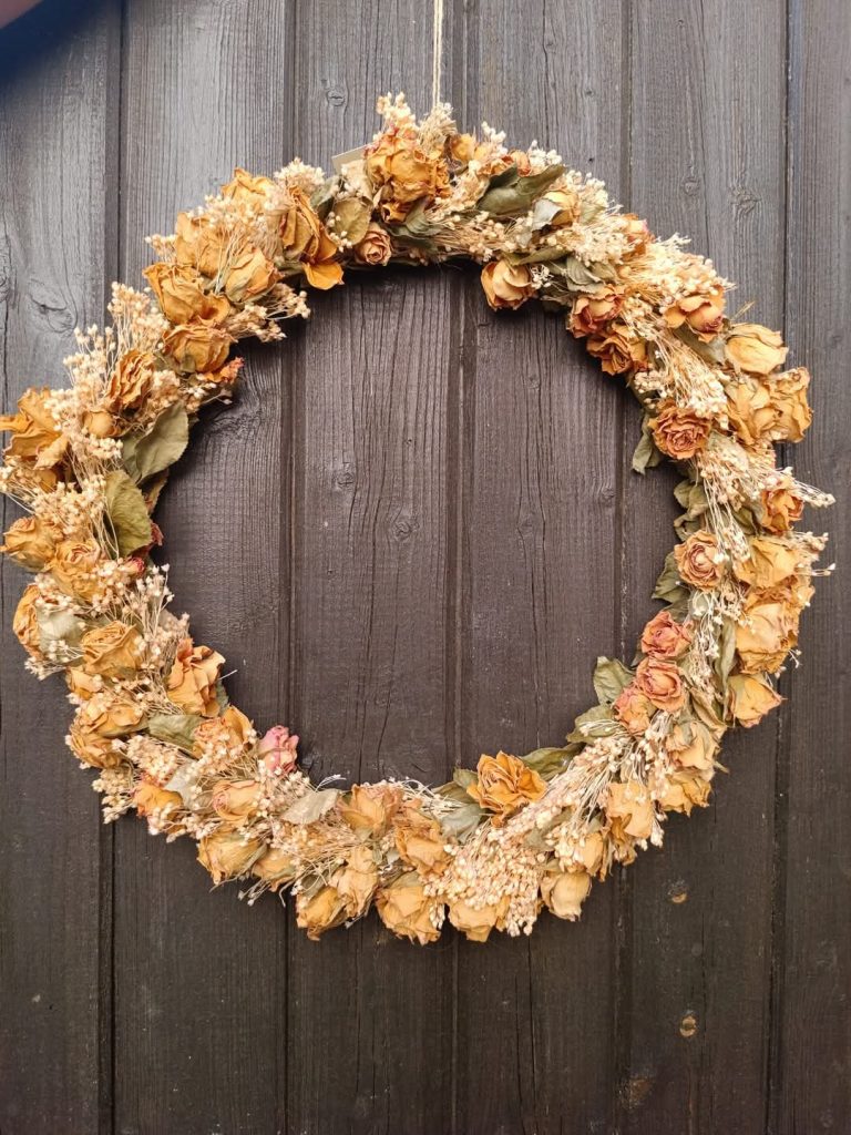 Une couronne de fleurs séchées orange suspendue après un mur en bois foncé pour décorer un baptême