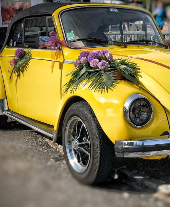 Une voiture coccinelle jaune décorée de fleurs par les fleuristes Un Brin d'Folie pour un mariage dans les Vosges