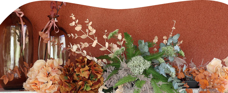 Une étagère en bois placé sur un mur orange terracotta et recouverte de fleurs, plantes et vases dans des tons verts et oranges
