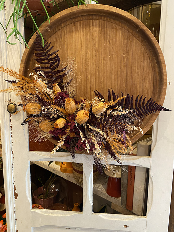 Une création artisanale sur mesure faite d'un plateau en bois recouvert de fleurs et plantes séchées, le tout accroché sur une veille porte en bois