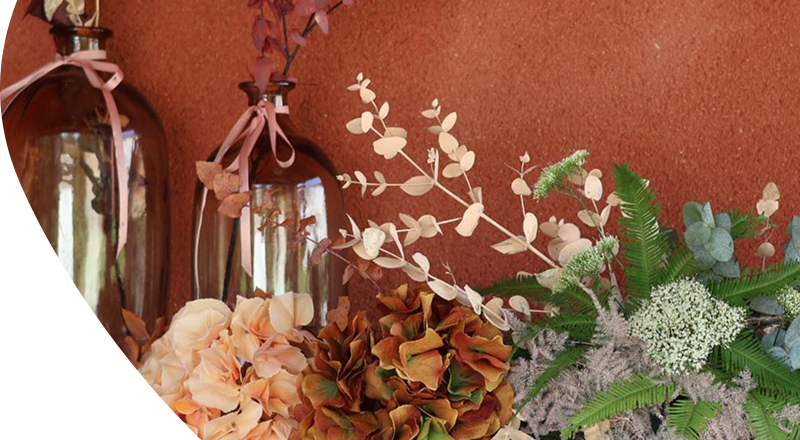 Décoration : Fleurs et plantes dans les tons oranges et verts placés devant un mur crépis couleur terracotta