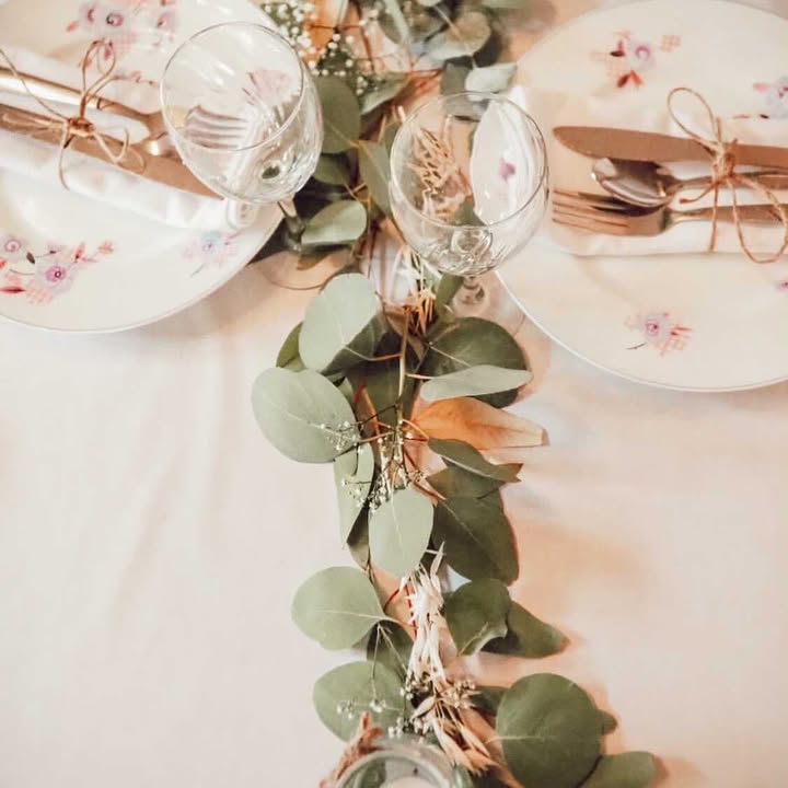 Une guirlande d'eucalyptus traverse une table entre les verres et assiettes pour un mariage dans les Vosges