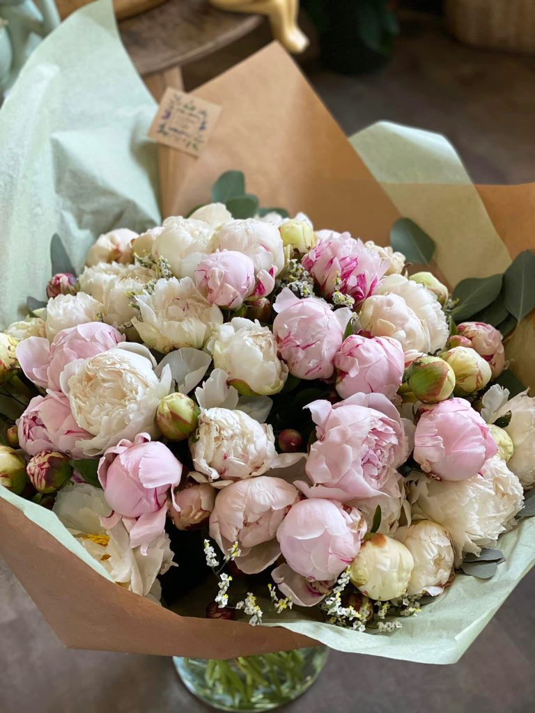 Un gros bouquet de pivoine roses et blanches emballé dans du papier de soie