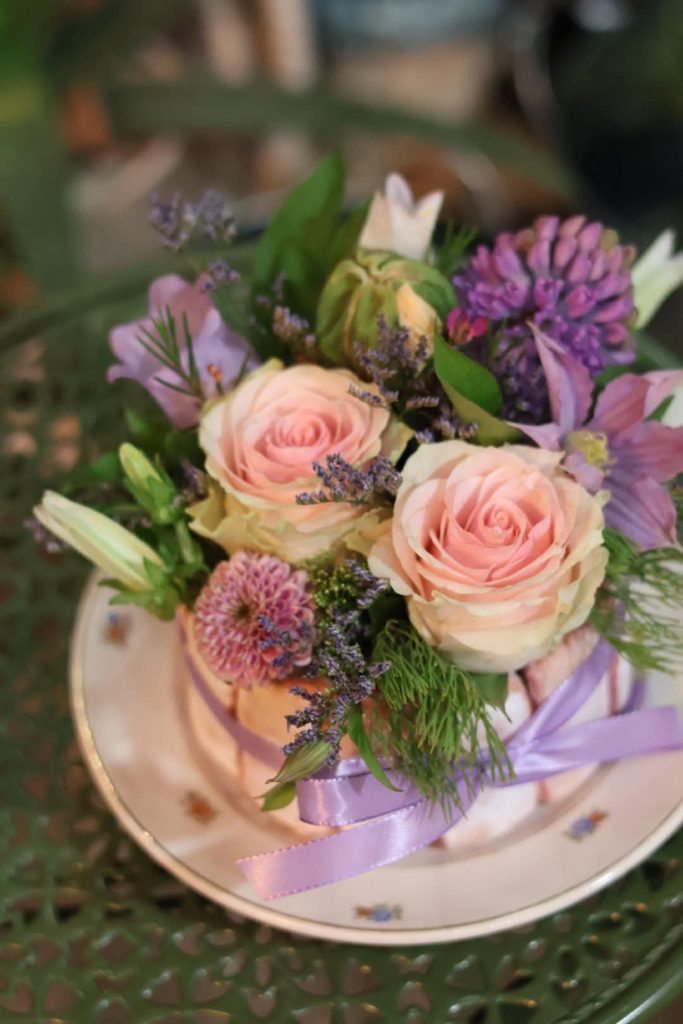 Une composition de fleurs fraîches dans les tons roses et violets dans une assiette avec de faux gateaux boudoirs