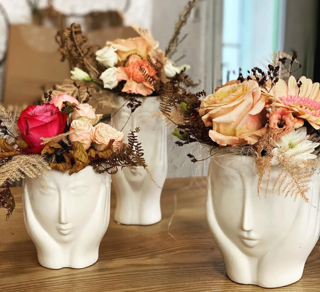 Décoration : Trois vases blancs originaux en forme de visages tenus entre les mains, garnis de fleurs fraîches et séchées