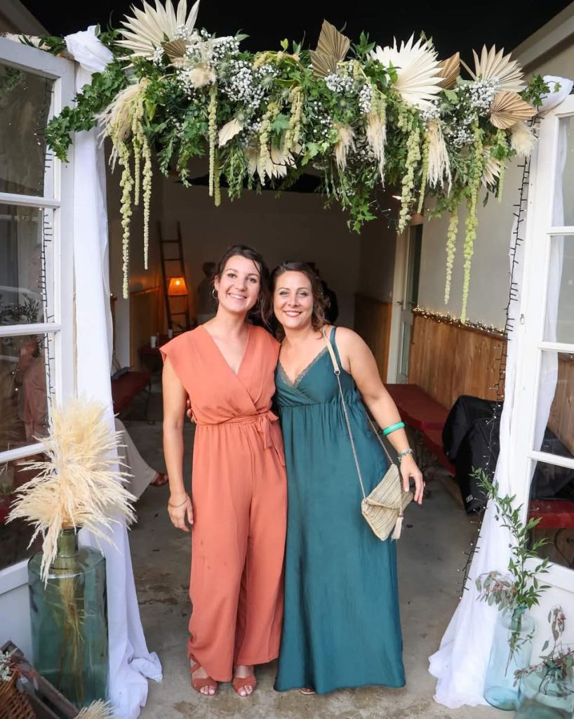 Les deux fleuristes Pauline et Sabrina sont en jolies robes à un mariage sous une arche fleurie qu'elles ont réalisé