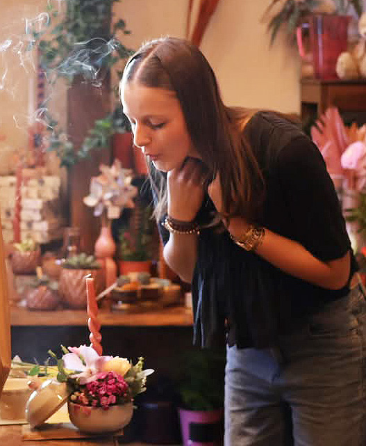 Photo de l'apprentie fleuriste Jade en train de souffler une bougie pour son anniversaire dans la boutique Un Brin d'Folie à Arches