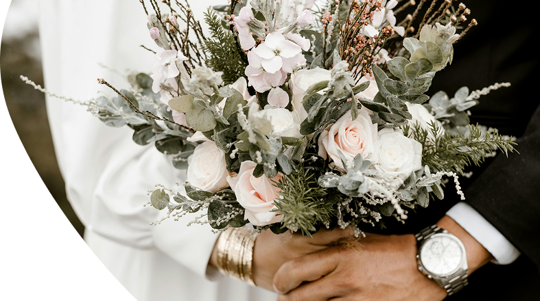 Une bouquet de mariée tenu par les mains des mariés qu'on aperçoit