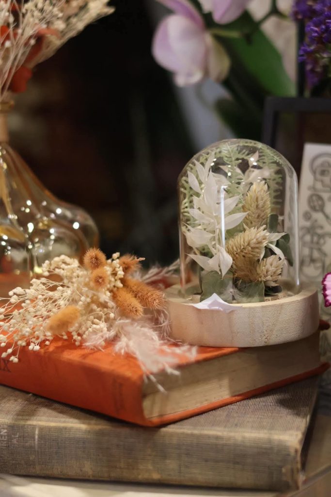 Deux livres superposés avec dessus des fleurs séchées et une cloche en verre décorative
