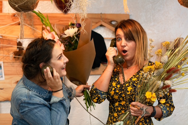 Les deux fleuristes répondent au téléphone dans une ambiance joyeuse et tiennent chacune un bouquet à la main