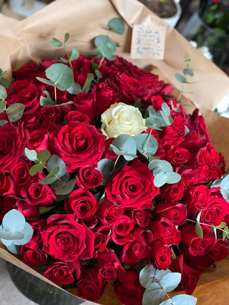 Un magnifique bouquet de 100 roses rouges dont une blanche au centre du bouquet et quelques branches d'eucalyptus