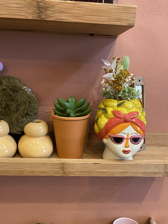 Plusieurs vases et pots sur une étagère en bois dont un original très coloré en forme de visage de femme avec des lunettes de soleil