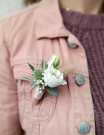 Une boutonnière de marié composé d'une petite rose blanche, portée sur la veste rose de la fleuriste Sabrina