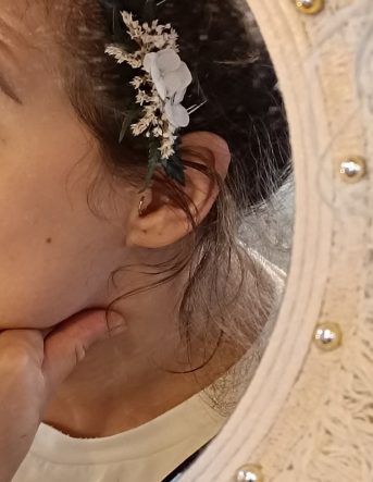 La fleuriste Pauline est devant un miroir avec un barrette fleurie crée sur mesure dans les tons blancs