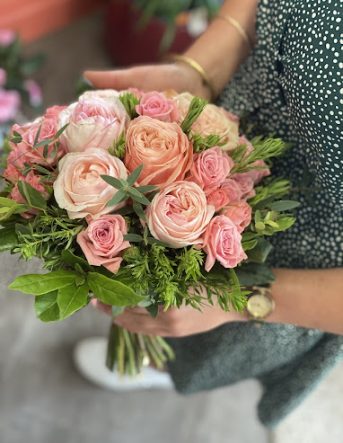 Les mains de fleuriste tiennent un joli bouquet de roses fraîches avec du feuillage vert pour un baptême à Arches