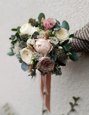 Un bouquet de mariée dans des tons très doux rose pastel et vert, attaché par un ruban rose qui retombe