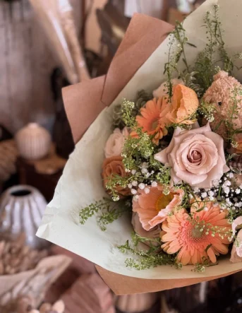 Un bouquet de fleurs rose et orange emballé dans du papier kraft et papier de soie assortit
