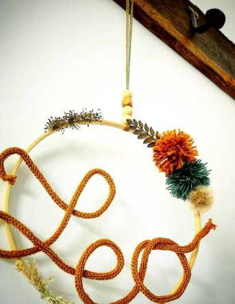 Couronne murale artisanale avec le prénom « Léo » formé en corde, décorée de fleurs séchées et pompons, crée pour une naissance à Arches