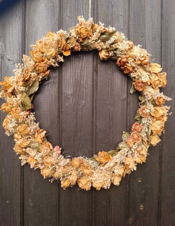 Une couronne de fleurs séchées orange suspendue après un mur en bois foncé pour décorer un baptême