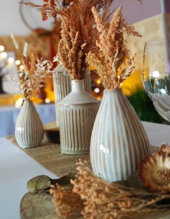 Des vases composés de fleurs séchées oranges sont placés au centre d'une table décorée pour un mariage dans les Vosges