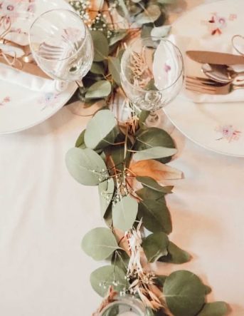 Une guirlande d'eucalyptus traverse une table entre les verres et assiettes pour un mariage dans les Vosges
