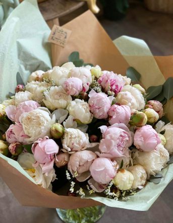 Un gros bouquet de pivoine roses et blanches emballé dans du papier de soie