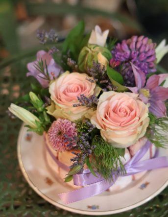 Une composition de fleurs fraîches dans les tons roses et violets dans une assiette avec de faux gateaux boudoirs