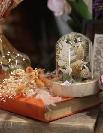 Deux livres superposés avec dessus des fleurs séchées et une cloche en verre décorative