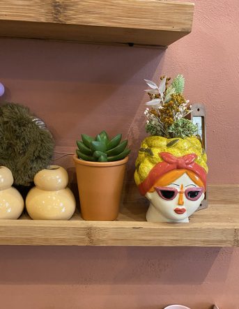 Plusieurs vases et pots sur une étagère en bois dont un original très coloré en forme de visage de femme avec des lunettes de soleil